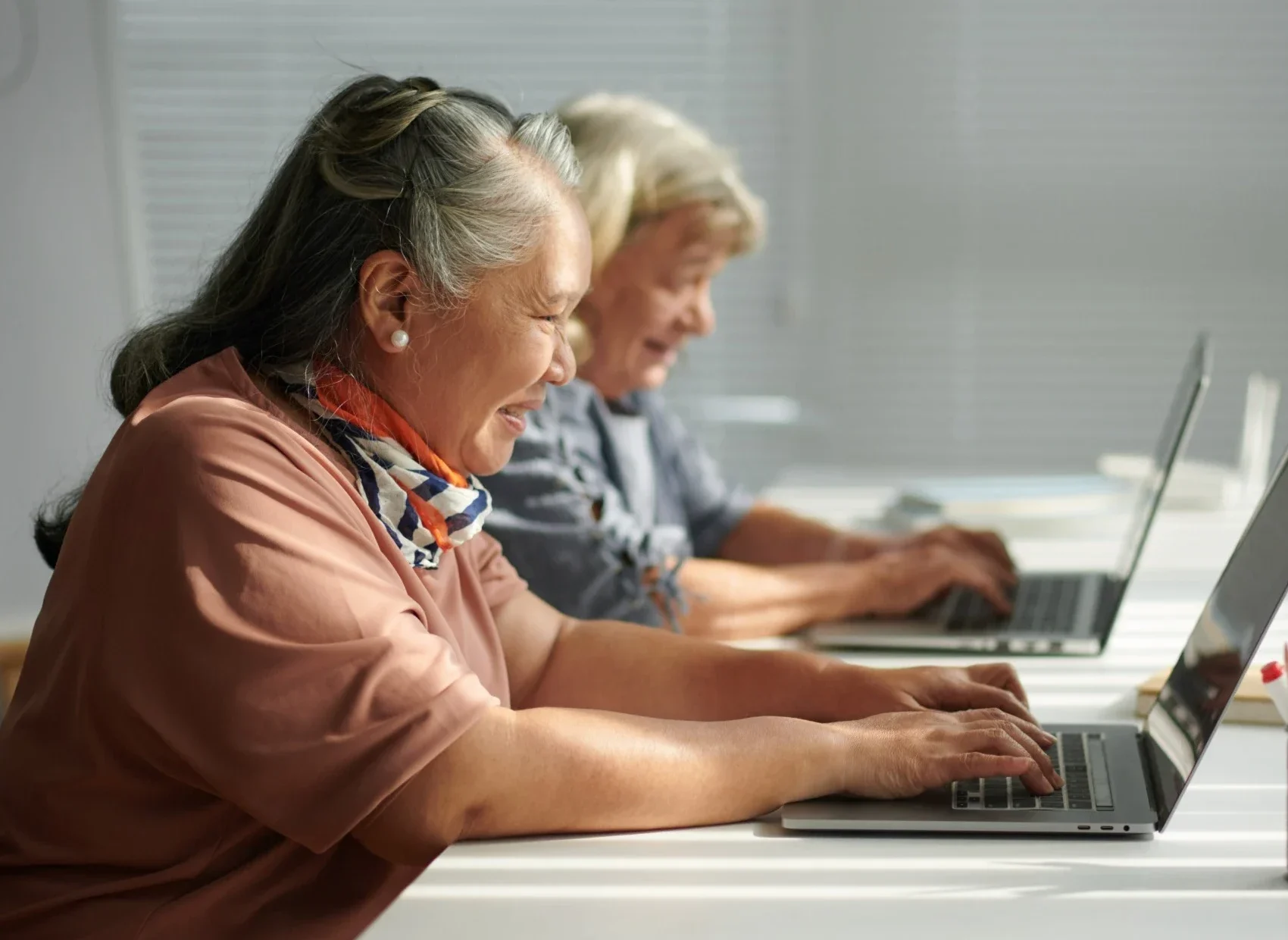 Two older women using laptops at desk