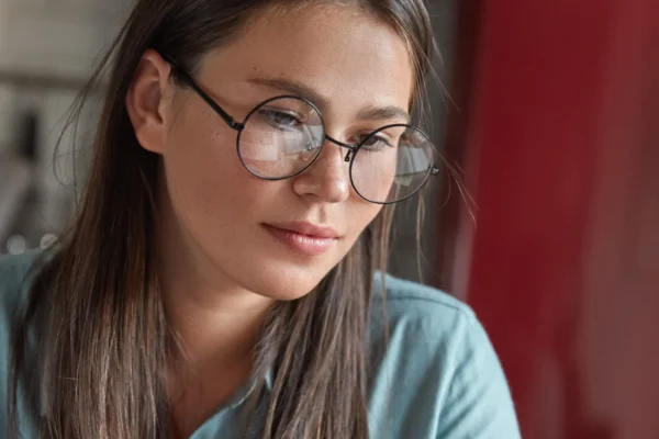 Woman wearing glasses reading document at laptop