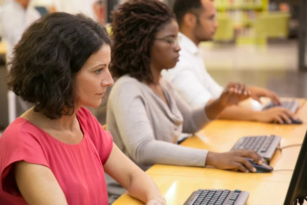 Adults working on desktop computers in library